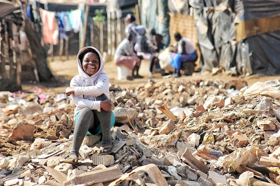 Hymyilevä lapsi istuu slummin roskakasassa.