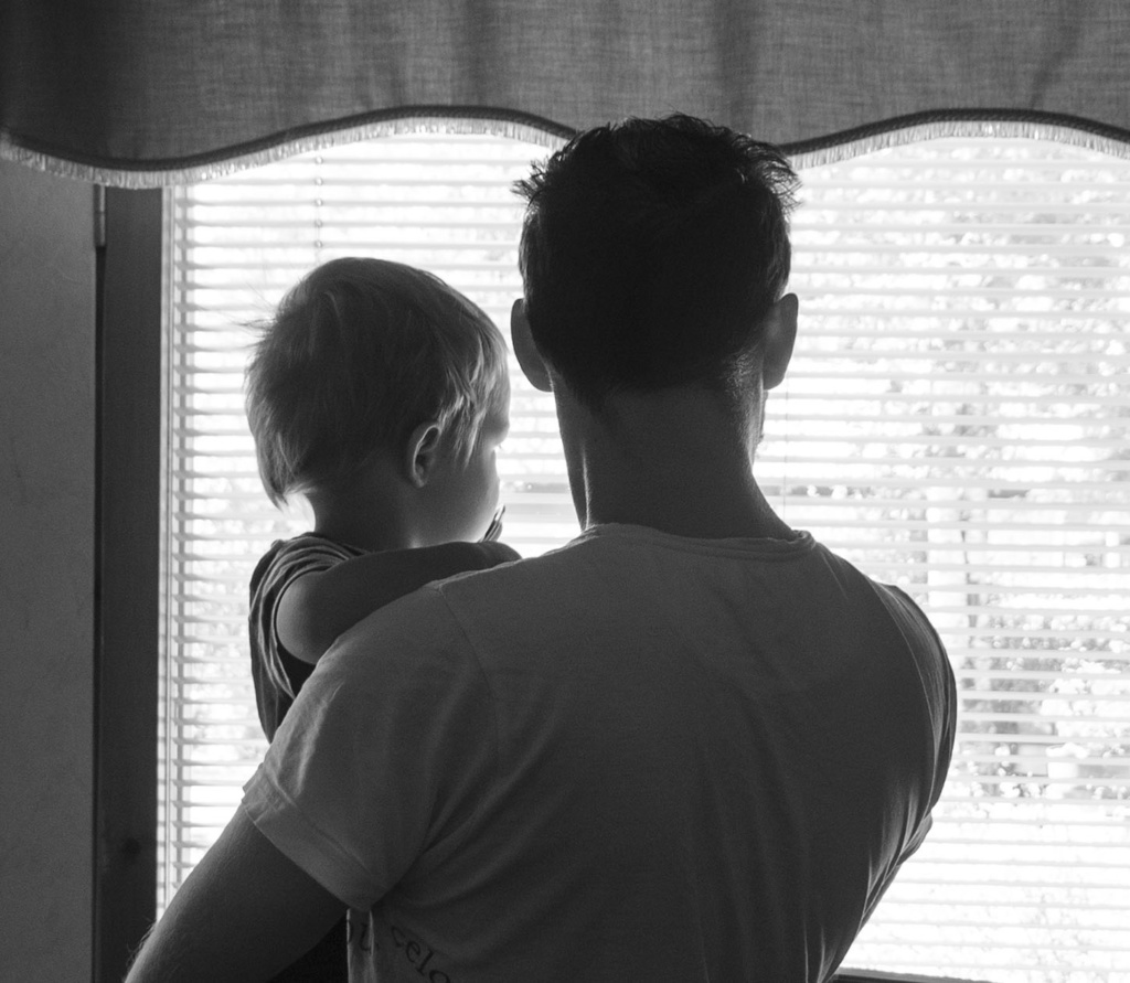 Isä ja hänen sylissään oleva lapsi katsovat selin ikkunasta ulos.