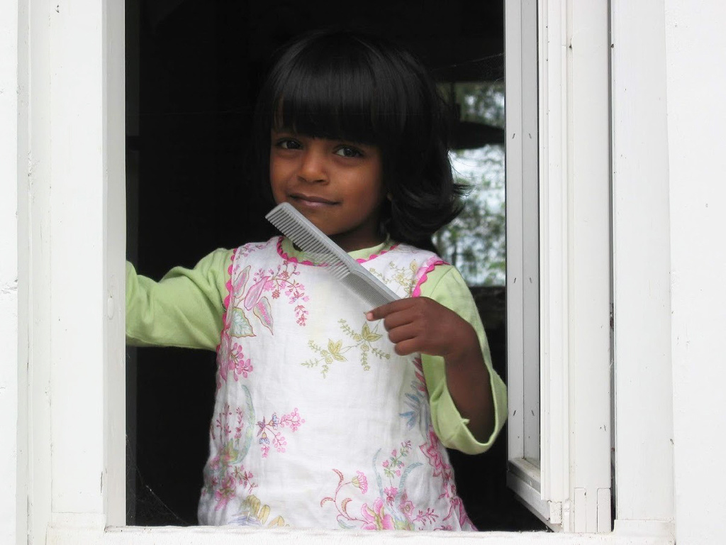 Pieni tyttö katsoo ikkunasta ulos kampa kädessä.