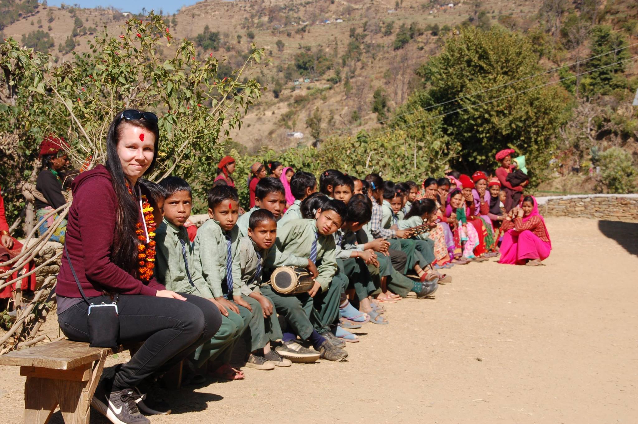 Nainen istuu penkillä nepalilaisten koululaisten kanssa.