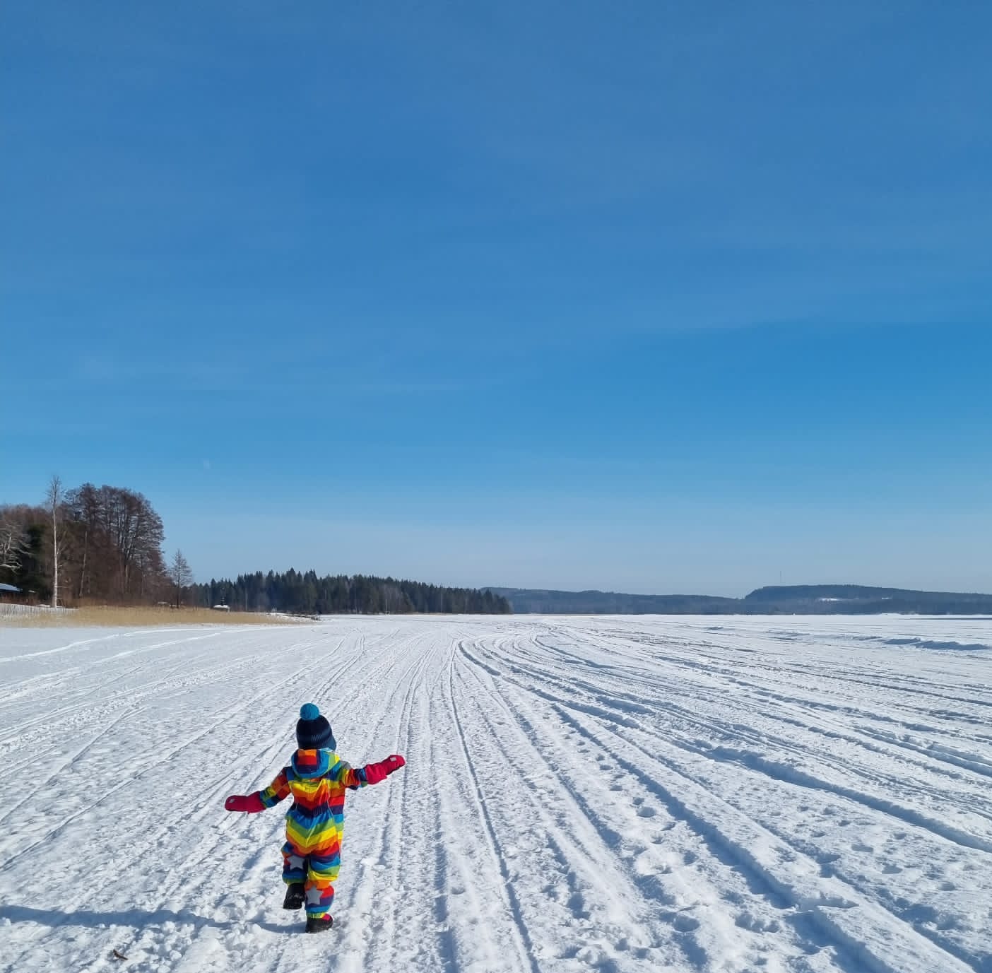 Lapsi selin lumisen järven jäällä aurinkoisessa säässä