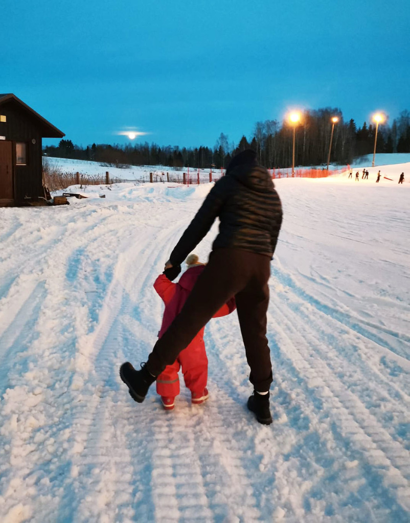 Vanhempi tukee taaperon kävelya lumimaisemassa