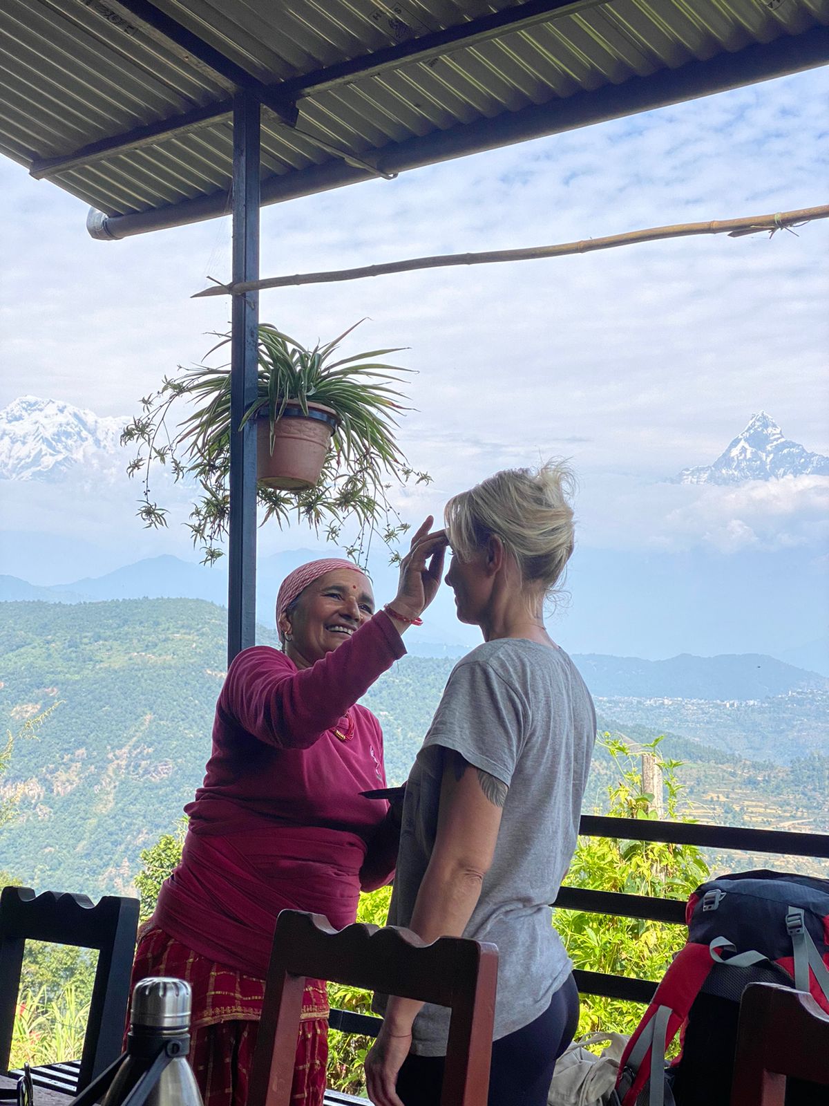Nepalilainen vanha nainen piirtää tikaa suomalaisnaisen otsaan, taustalla vuoristomaisema