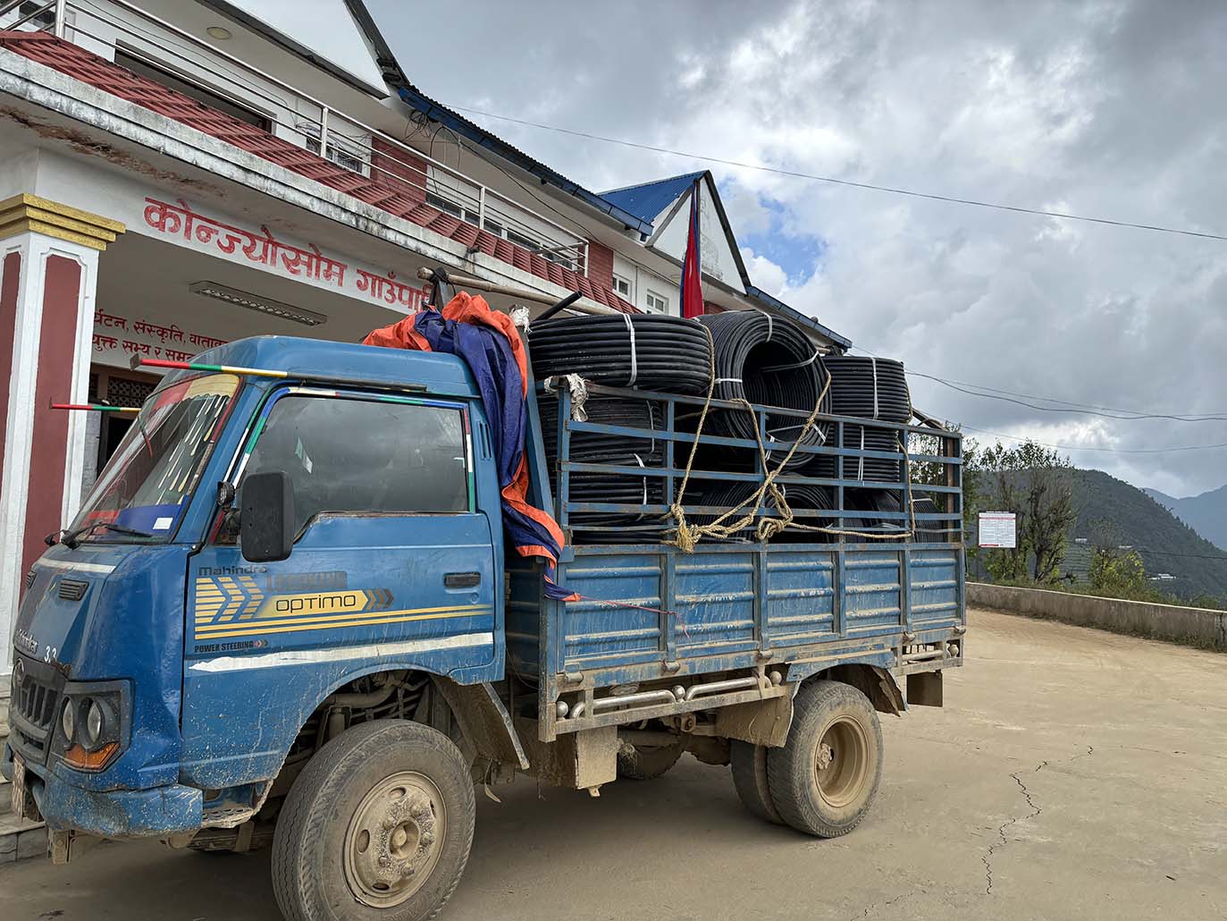 Nepalilaisen rakennuksen edessä on kuorma-auto, jonka lavalla on vesijohtoja