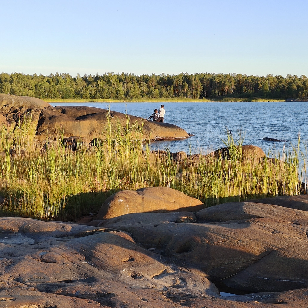 Kaksi lasta näkyy kaukana kivisellä rannalla auringonlaskun aikaan